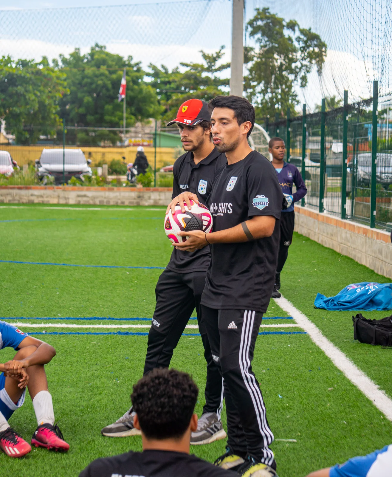 Highlights coach speaking to young participants during a soccer clinic