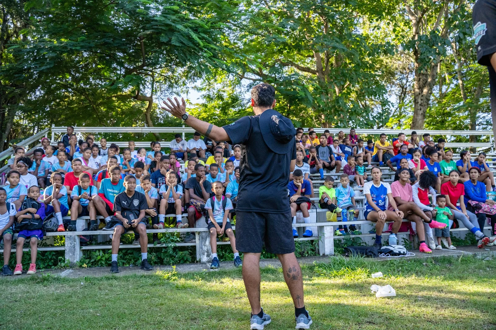 Coach addressing a large group of children at an outdoor soccer clinic